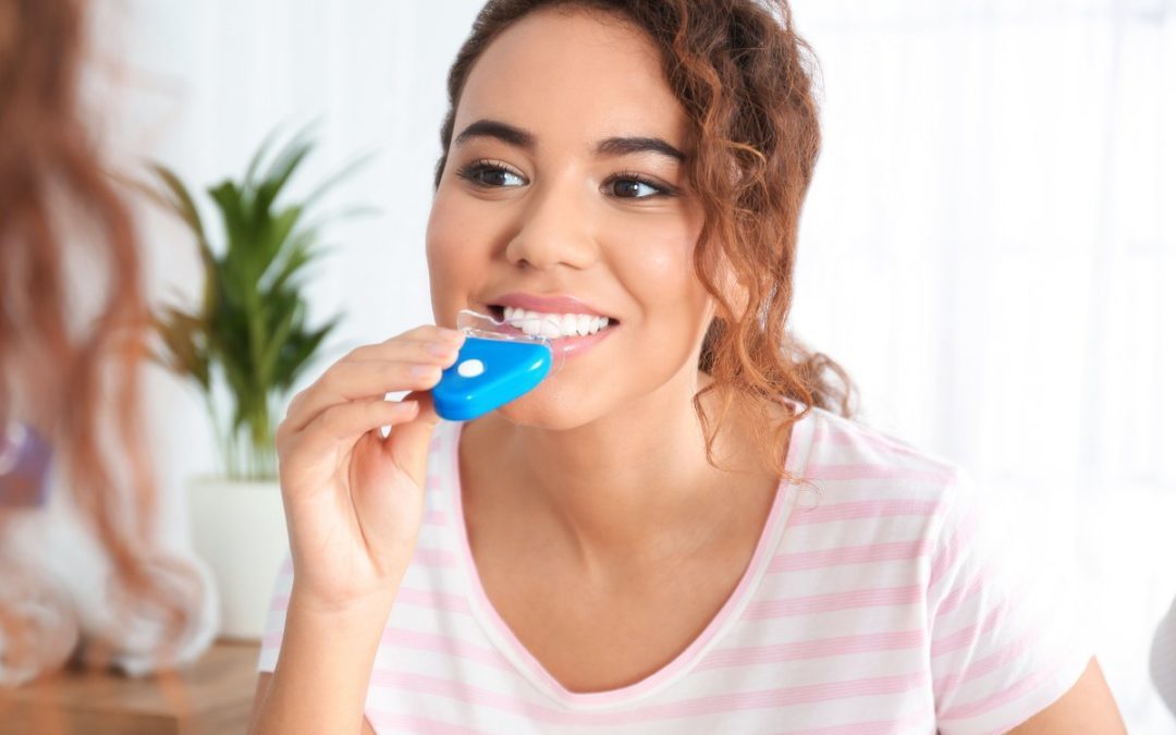 Young woman brushing teeth with blue toothbrush in bright bathroom setting.