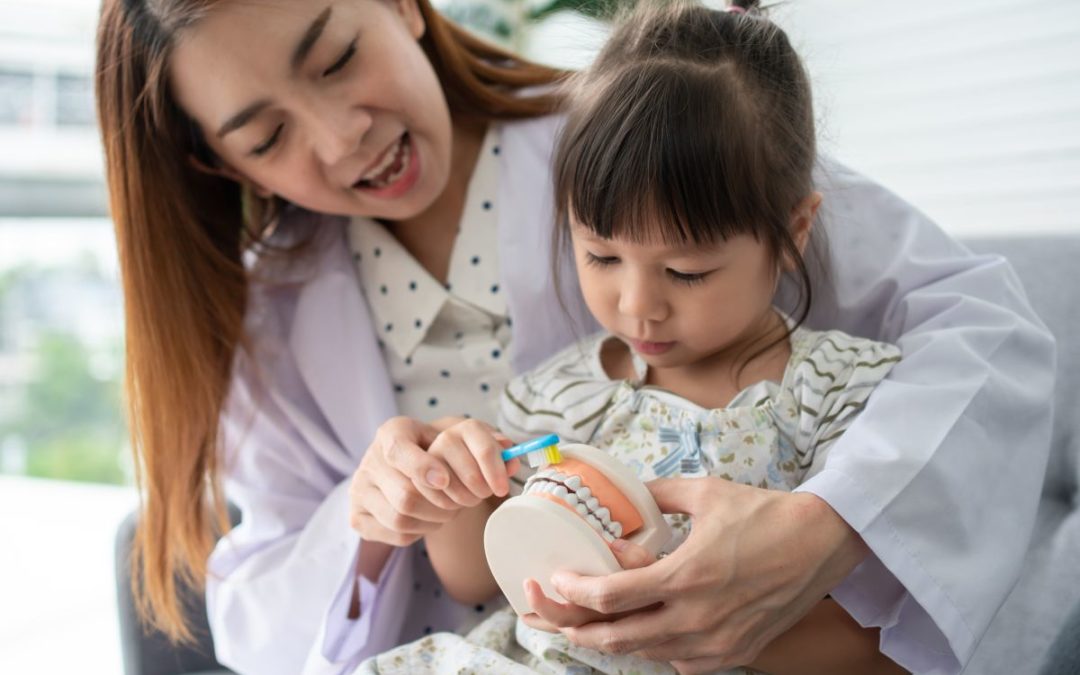 Adult and child examining a tooth model together in a bright dental office setting.