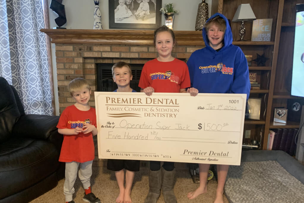 Family holding large Premier Dental charitable donation check in home living room setting.